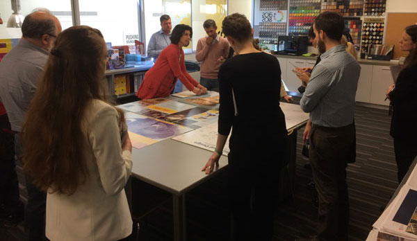 a group stands at a table filled with example museum panels made of metal, fabric, and acrylic