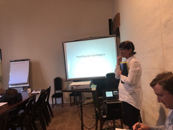 woman in a white blouse stands in front of a projection of the Spanish words Planificacion Estrategia 