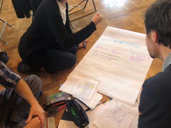 a large piece of paper with colored marker notes in Spanish. arms and legs of the people working on it are visible