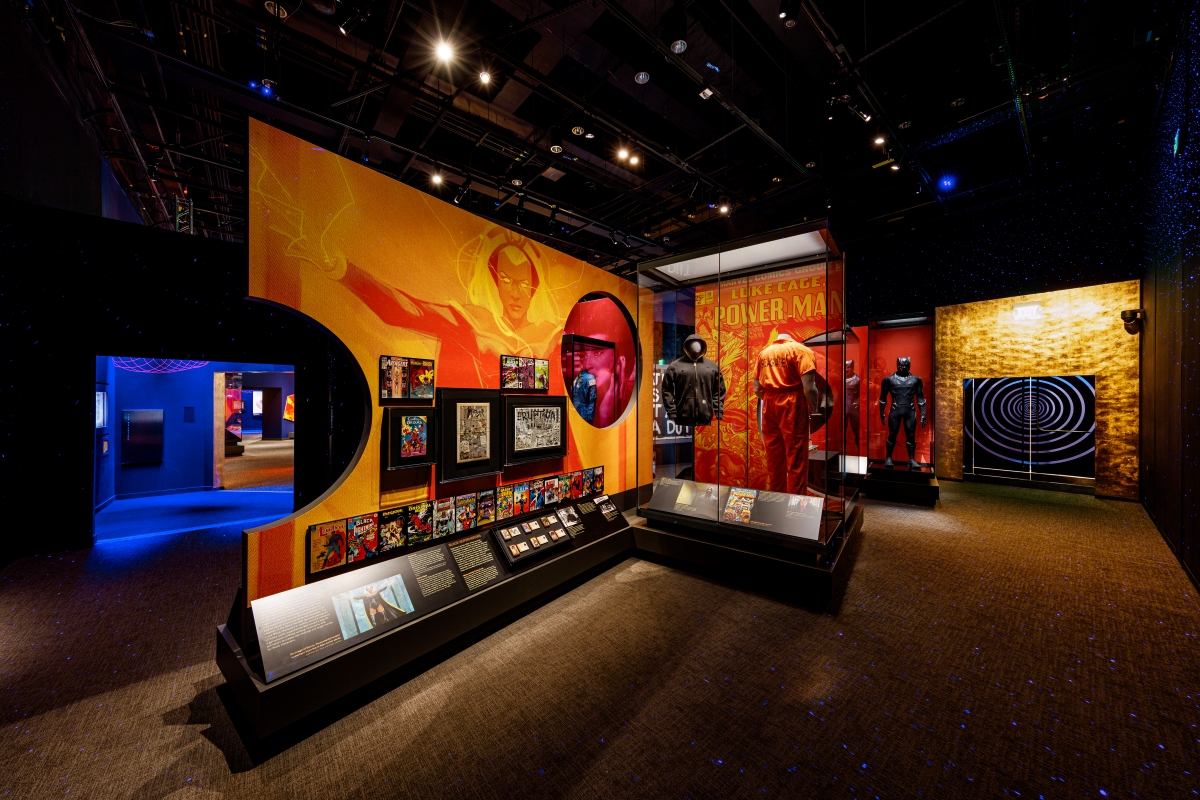 An orange-tinted graphic mural next to a display case shows a Black superhero.