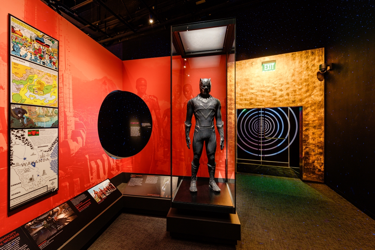 A display case features a black superhero costume against a red background.