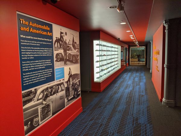 A view of a red hallway showing a graphic panel and a backlit display case